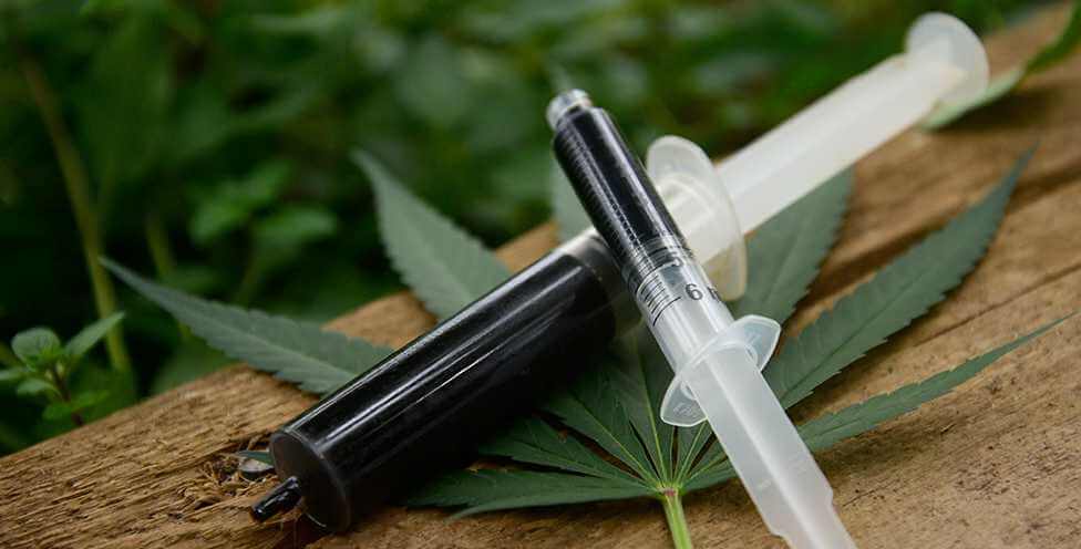 RSO applicators on top of a cannabis leaf, sitting on a wooden surface