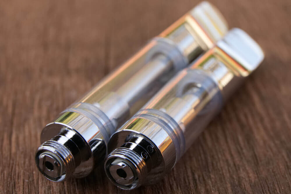 Two silver cannabis vape cartridges on wooden surface