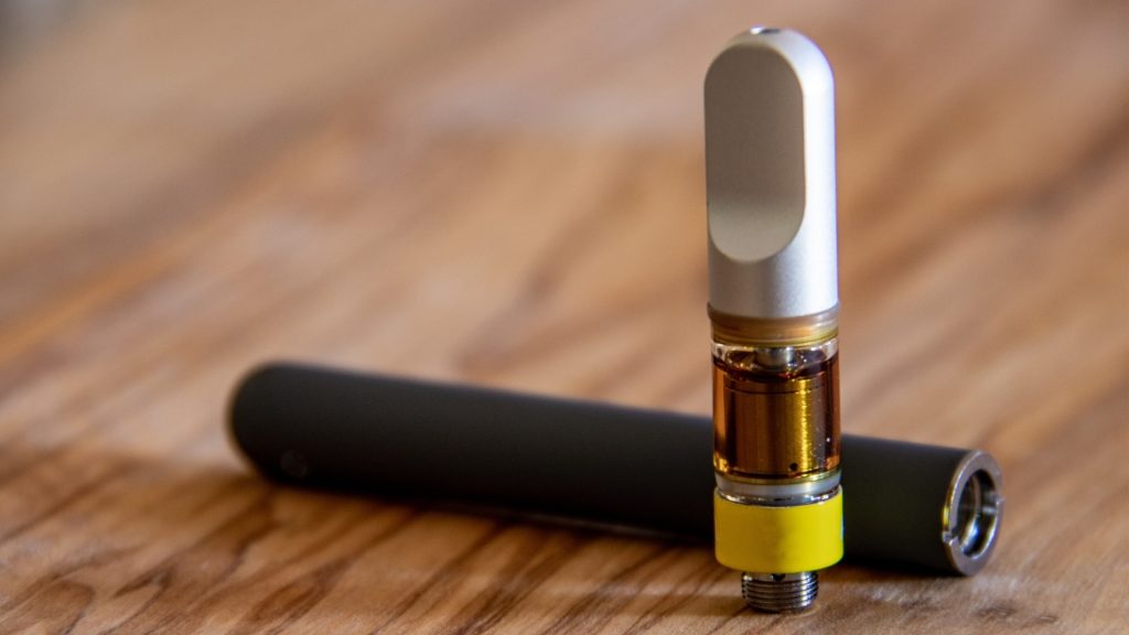 Cannabis vape cartridge and separate black battery on wooden surface