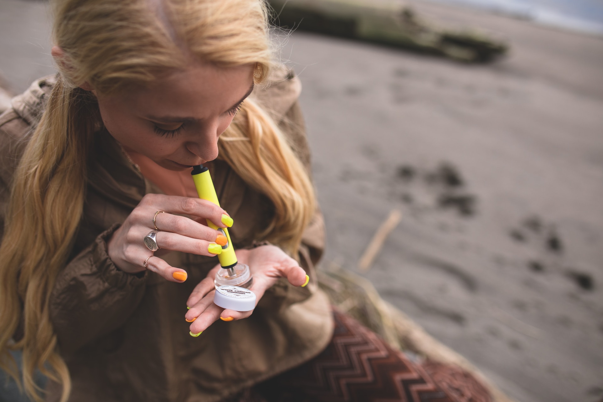A woman with blonde hair uses a yellow Dip Devices electronic dabber to consume hash rosin.