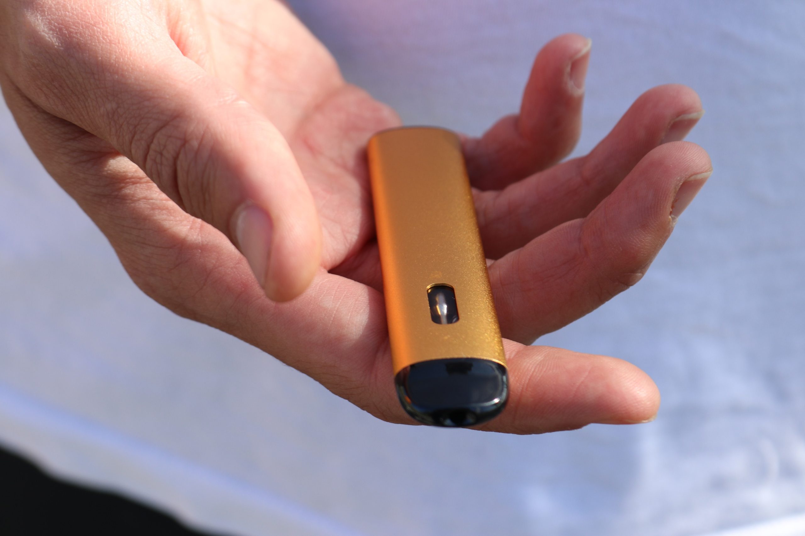 An orange vape pen is placed in an open hand. It's an illustration of the several cannabis vape types available for purchase in New Jersey.