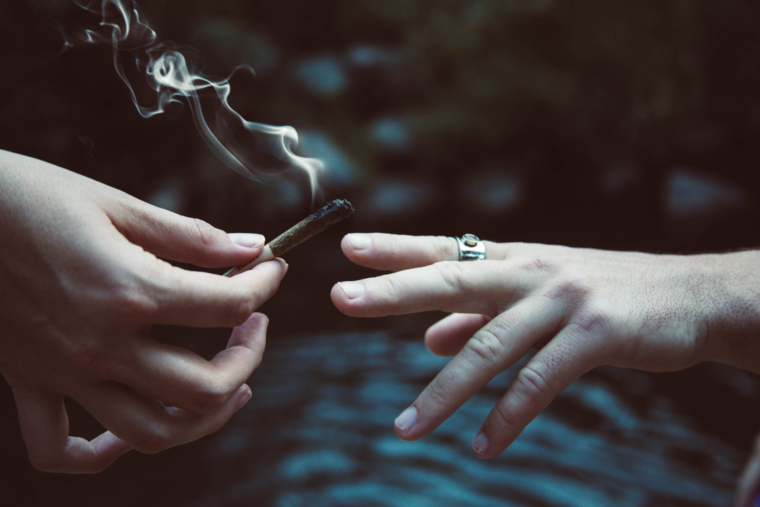 A close-up of two white hands passing a joint from one to another. There is a ring on one of the hands.