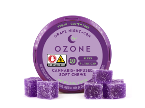 A container of Ozone edibles is depicted on a white background. The tin is purple, with a light purple label with dark purple writing. Five square edibles with sugar coating can be seen outside the package.