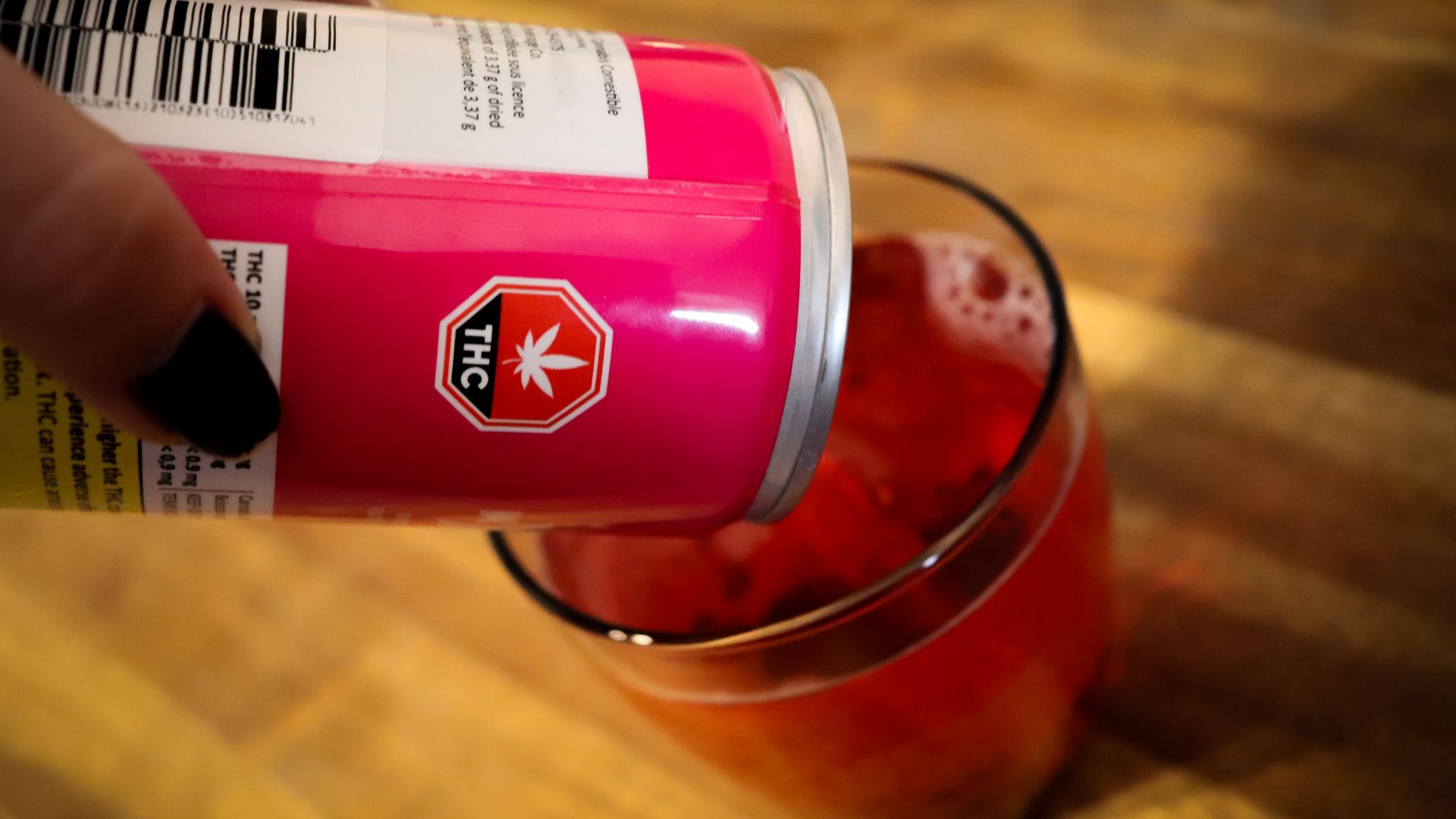 A THC beverage in a pink can is being poured into a glass.