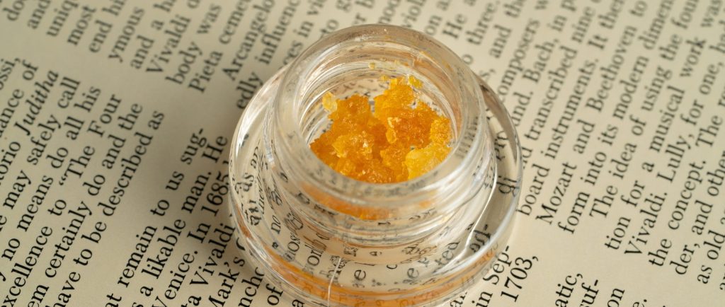 Clear jar of yellow cannabis concentrate on book page background