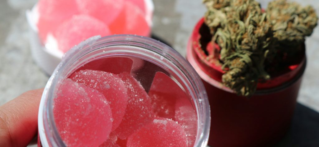 Pink THC edibles in jar with cannabis flower in background