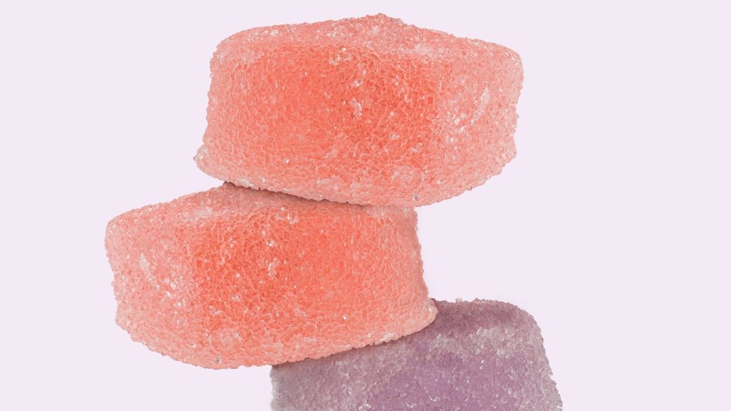 Stacked pink and purple cubed cannabis edibles in front of light purple background