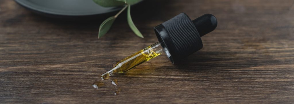 Pipette filled with cannabis tincture on brown wooden table