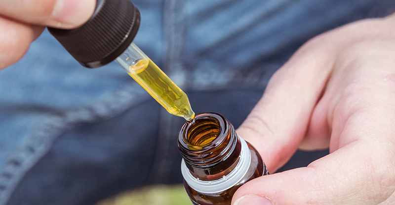 Hands holding dropper of yellow cannabis tincture