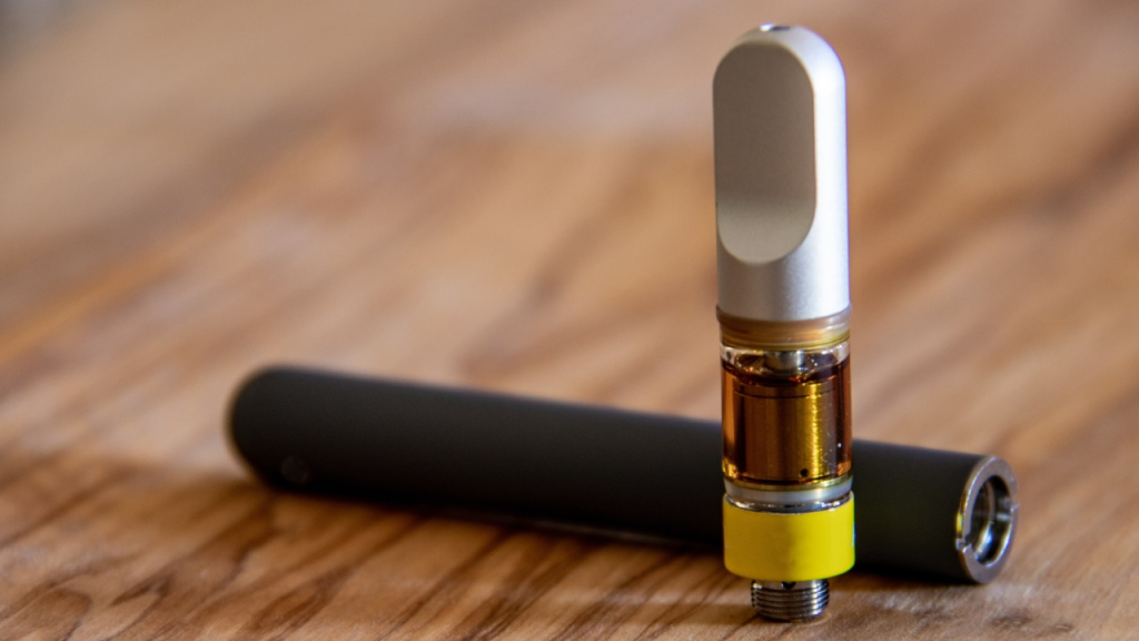 Close-up of a THC vape cartridge and pen on a wooden surface, highlighting oil levels and functionality for Queen City Dispensary's blog on vape FAQs.