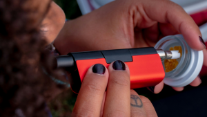 A person using a red dab pen to vaporize cannabis concentrate from a glass jar.