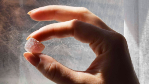 A close-up of a hand holding a sugar-coated cannabis gummy against natural light.